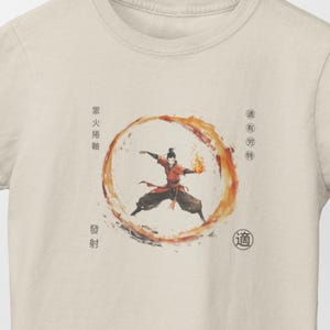 May include: A beige t-shirt with a graphic print of a character from the animated series Avatar: The Last Airbender. The character is surrounded by a ring of fire and the text "燃火相融" and "道" are printed on the shirt.