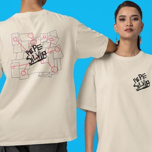 May include: Cream-colored t-shirt with the text "PEPE SILVIA" in black on the front and back. The back of the shirt features a graphic of connected papers and circles in black and red.