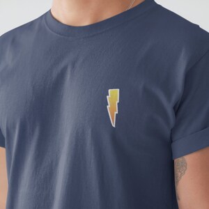 Puede incluir: Una camiseta azul marino con un gráfico de rayo amarillo y naranja.