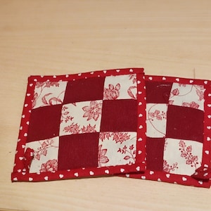 Peut inclure: Deux dessous-de-verre en tissu matelassé rouge et blanc avec un motif de cœur blanc sur les bords.