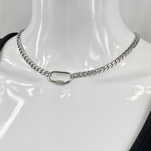 May include: A silver curb chain necklace with a carabiner clasp. The necklace is displayed on a white mannequin. The chain links are closely spaced, and the clasp is an oval shape with a screw closure.