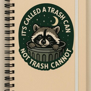 May include: Spiral-bound notebook with a tan cover and a white elastic band. The cover features a circular design with a raccoon peeking out of a trash can, surrounded by the text "IT'S CALLED A TRASH CAN NOT TRASH CANNOT."