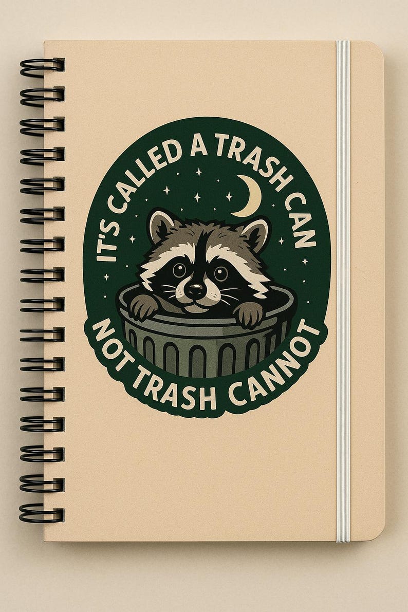 May include: Spiral-bound notebook with a tan cover and a white elastic band. The cover features a circular design with a raccoon peeking out of a trash can, surrounded by the text "IT'S CALLED A TRASH CAN NOT TRASH CANNOT."