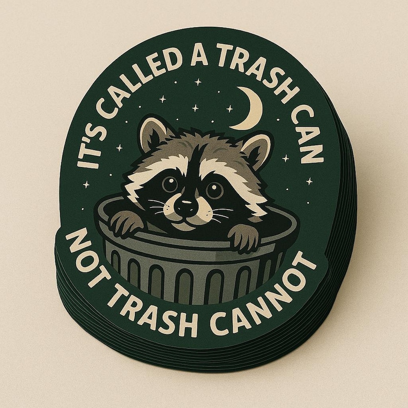 May include: A stack of round stickers with a raccoon peeking out of a trash can. The stickers are dark green with white text that reads "IT'S CALLED A TRASH CAN NOT TRASH CANNOT". A crescent moon and stars are also featured.