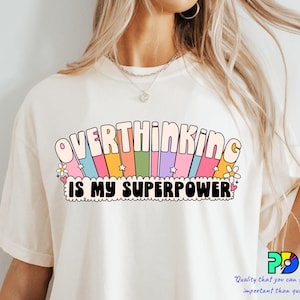 May include: White t-shirt with a rainbow graphic and the text "Overthinking is my superpower".