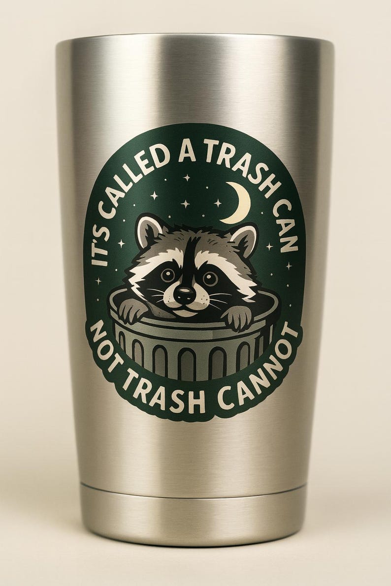 May include: A stainless steel tumbler with a green and white graphic of a raccoon peeking out of a trash can. The text on the tumbler reads "It's called a trash can, not trash cannot."