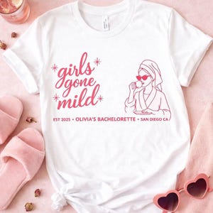 May include: White t-shirt with a pink graphic that reads "girls gone mild" with a drawing of a woman in a robe and sunglasses. The shirt also includes the text "EST 2025 • OLIVIA'S BACHELORETTE • SAN DIEGO CA".
