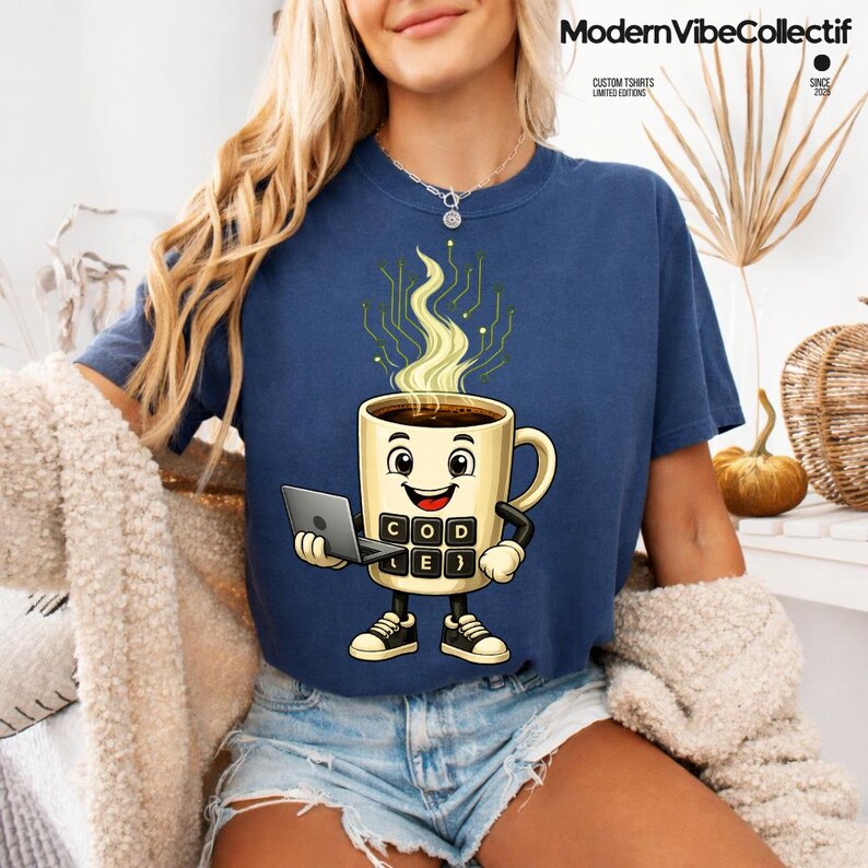 Pu&ograve; includere: Una t-shirt blu navy con un personaggio a forma di tazza di caff&egrave; sorridente che tiene in mano un piccolo computer portatile. La tazza presenta un design a tastiera sul davanti ed emette vapore giallo a forma di circuito. Girocollo e maniche corte.