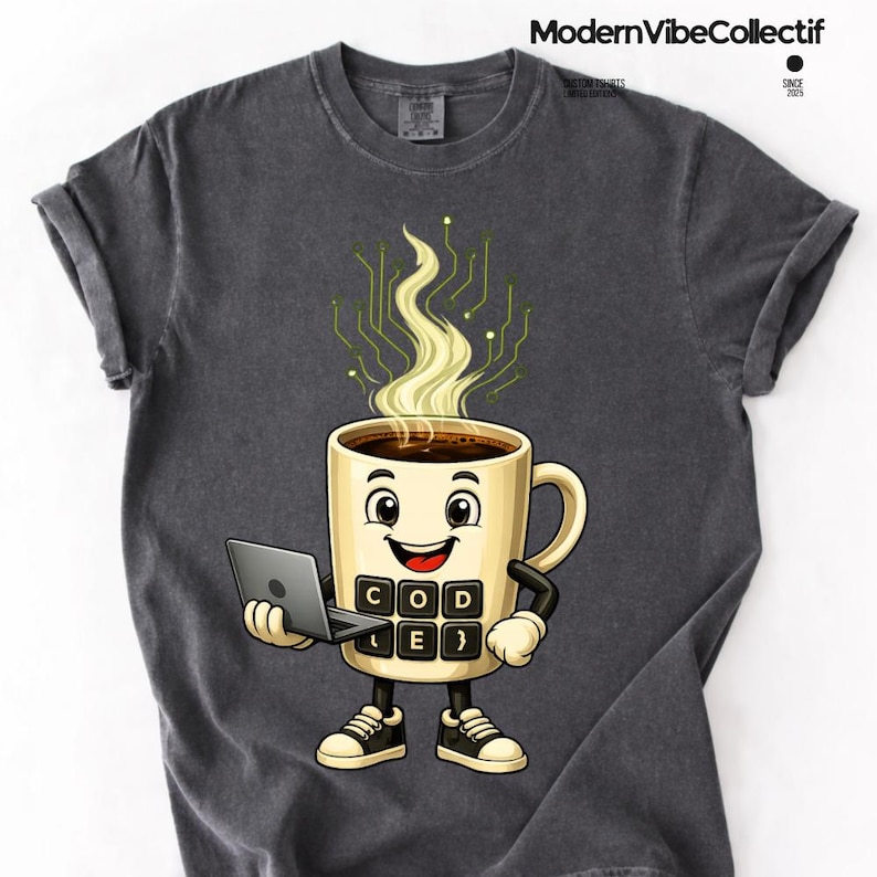 Pu&ograve; includere: Una t-shirt grigio antracite con un personaggio a forma di tazza da caff&egrave; che tiene un portatile. La tazza ha un volto, braccia, gambe e un tastierino con la scritta "CODE". Il vapore forma un motivo a circuito stampato verde.