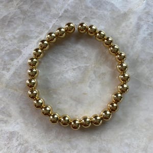 May include: A gold beaded bracelet with a simple, classic design. The bracelet is made of small, round beads that are strung together to form a circle.