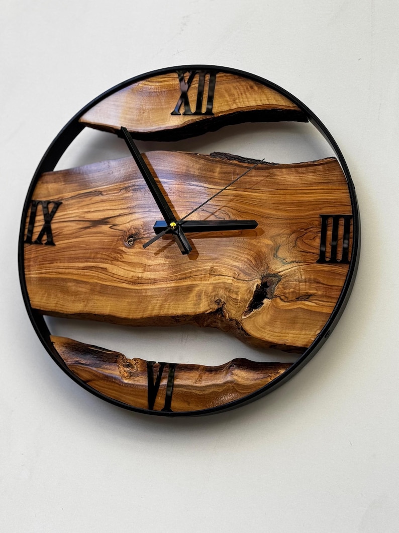 Handmade olive wood wall clock featuring natural live edge wood slabs, black metal frame, Roman numerals, and unique organic wood grain patterns, perfect for rustic, farmhouse, and modern home decor.