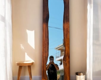 May include: A full-length mirror with a natural wood frame. The frame has a unique, irregular shape with a live edge design. The mirror is reflecting a person standing in front of it.