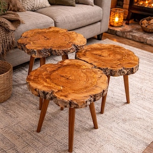 May include: Three rustic wooden side tables with natural, irregular edges and three wooden legs each. The tables have a warm, brown color and are arranged on a light-colored rug in a living room setting.