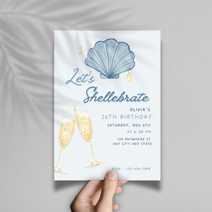 May include: A blue and white seashell illustration with gold stars and two champagne glasses. The text "Let's Shellebrate Olivia's 26th Birthday" is on the invitation. The invitation also includes the date, time, and location of the party.