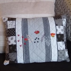 May include: A gray and white patchwork pillow with embroidered flowers in shades of red and orange. The pillow is quilted with a diamond pattern.