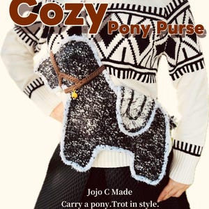 May include: A black and white pony-shaped purse with a brown halter and a yellow bell. The purse is worn over a white sweater with a black geometric pattern. The text "Cozy Pony Purse" is at the top, and "Carry a pony. Trot in style." is at the bottom.