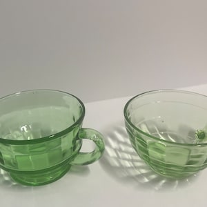 Può includere: Due tazze da tè in vetro verde con un design testurizzato. Una tazza ha un manico, l'altra no.