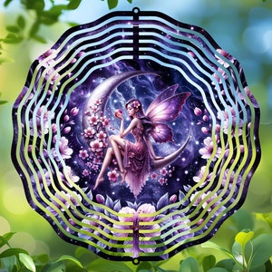 May include: A metal wind spinner with a purple fairy sitting on a crescent moon. The fairy has pink wings and is surrounded by pink flowers. The background is a dark blue with stars.