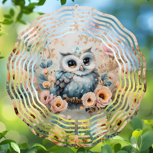 May include: A decorative owl wind spinner with a whimsical design. The owl is depicted with large eyes and surrounded by flowers in shades of pink and peach. The outer ring has a wavy pattern in pastel colors.