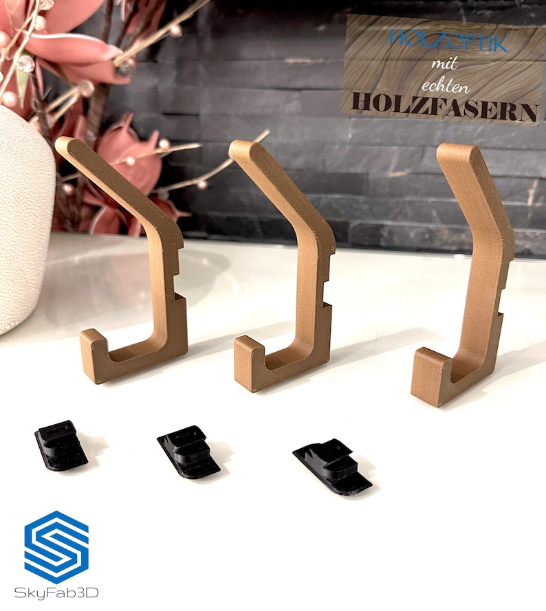 Auf dem Bild ist eine Einzelansicht von der Set-Option 3er-Set in Holzoptik aufgeführt. Es handelt sich um drei Doppelhaken in Holzoptik sowie drei Klemmsteine für die Montage ohne Bohren.
Auf dem Text oben rechts steht: "Enthält echte Holzfasern"