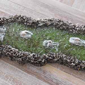 May include: A miniature stream bed with a waterfall and three small white fish. The stream bed is made of small stones and the water is clear and green.