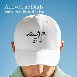 May include: White baseball cap with the text "Above Par Dad" in black script and a golfer silhouette. The hat is embroidered and has a relaxed fit. The background is a gradient of blue.