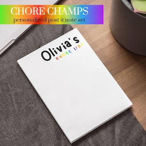 Puede incluir: Un bloc de notas blanco con el texto "Olivia's Chore List" en letras negras y arcoíris. El bloc de notas está sobre una superficie de tela gris.