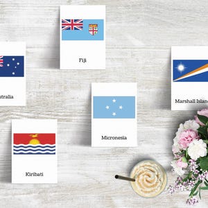 以下が含まれることがあります： オーストラリア、フィジー、ミクロネシア、キリバス、マーシャル諸島の国旗が描かれたカード。各カードには国旗のデザインと国名が記載されています。ピンクと白の花束とストローの付いた飲み物も画像にあります。