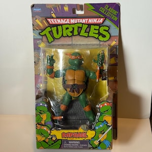 Könnte beinhalten: Eine Raphael-Actionfigur der Teenage Mutant Ninja Turtles in der Originalverpackung. Die grüne Figur trägt eine orangefarbene Maske und hat einen braunen Panzer. Die Verpackung trägt die Aufschrift "Teenage Mutant Ninja Turtles" und "Raphael".