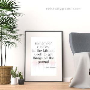 May include: A black framed print with a white background and black text that reads "remember cuddles in the kitchen yeah to get things off the ground - Arctic Monkeys". The text is accompanied by a pink sound wave graphic.