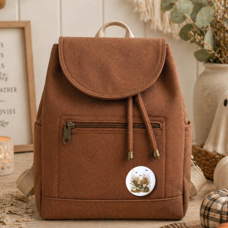 May include: A brown backpack with a flap closure and a front zippered pocket. The backpack has a drawstring closure and a small decorative pin with a floral design. The bag has a beige handle and straps.