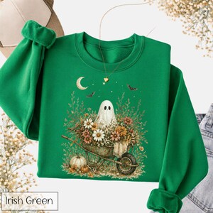May include: Irish green sweatshirt featuring a ghost in a wheelbarrow filled with flowers and a pumpkin. The design includes a crescent moon, stars, and bats. The text "Irish Green" is at the bottom.