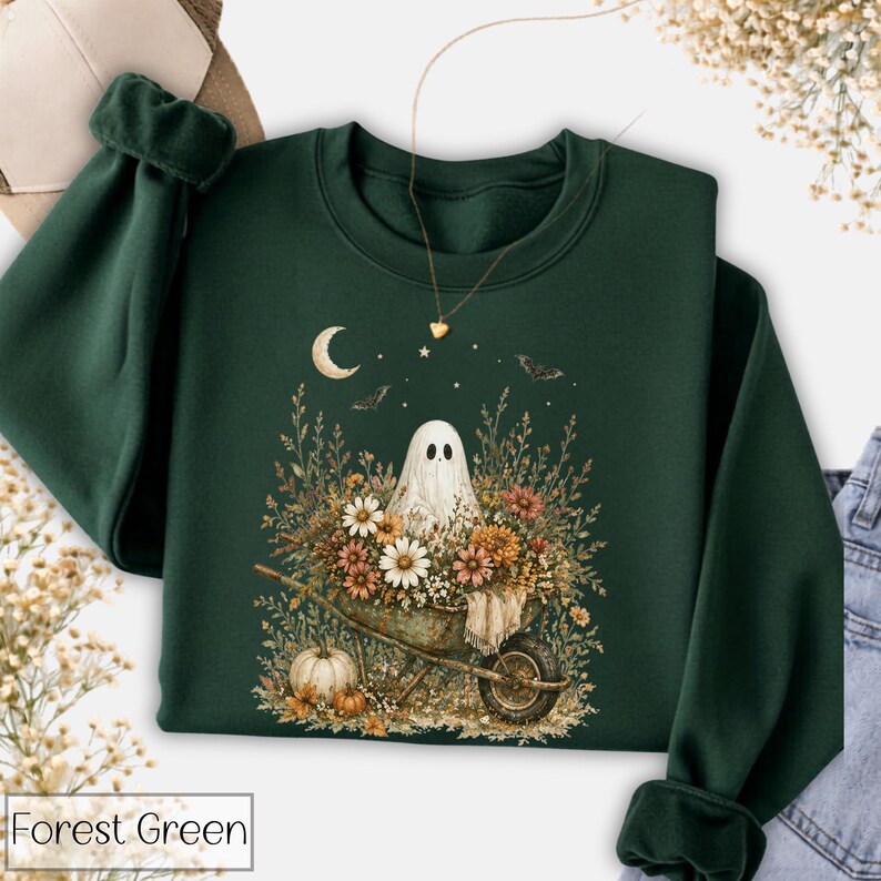 May include: Forest green sweatshirt featuring a ghost in a wheelbarrow filled with flowers and a pumpkin. The design includes a crescent moon, stars, and bats. The text "Forest Green" is at the bottom of the image.