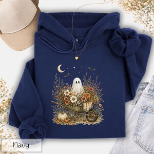 May include: Navy blue hoodie featuring a whimsical ghost design. The graphic includes a ghost in a wheelbarrow filled with flowers, a crescent moon, stars, and bats. The word "Navy" is printed at the bottom left.