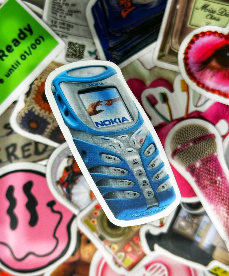 May include: A blue Nokia cell phone sticker with a white border. The phone has a digital display with a picture of two hands reaching towards each other. The phone has a keypad with the Nokia logo on the bottom.