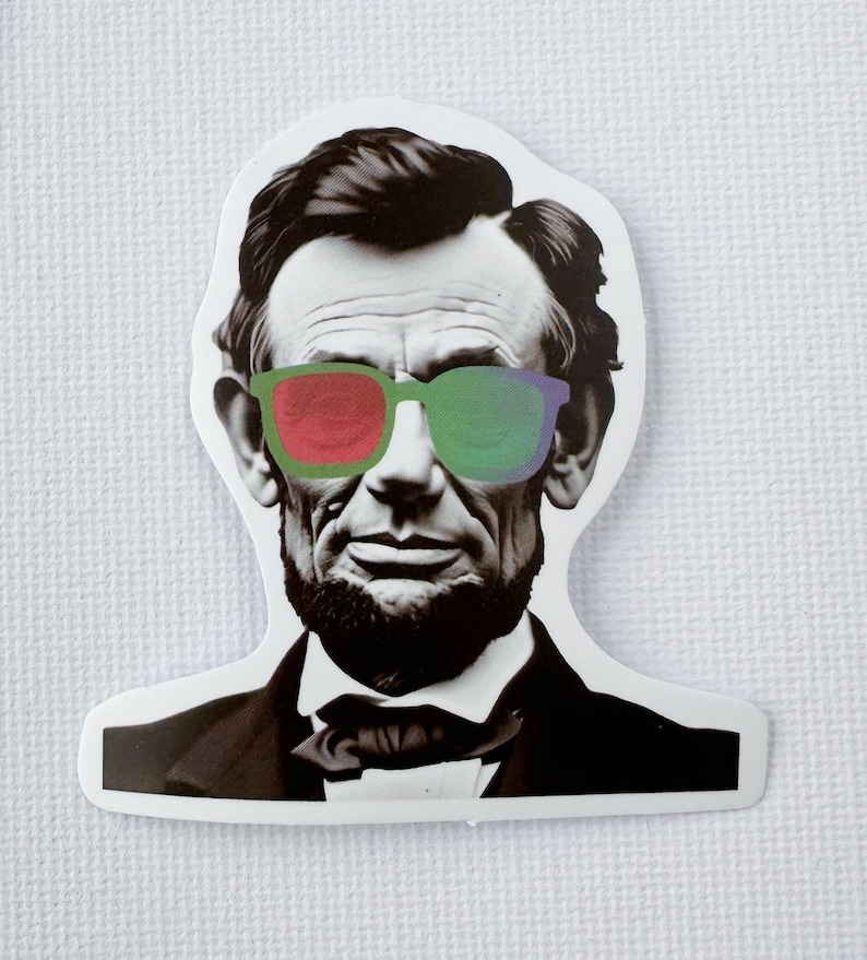 May include: A sticker depicting Abraham Lincoln in black and white, wearing sunglasses with red and green lenses. The sticker is cut to the shape of his head and shoulders.