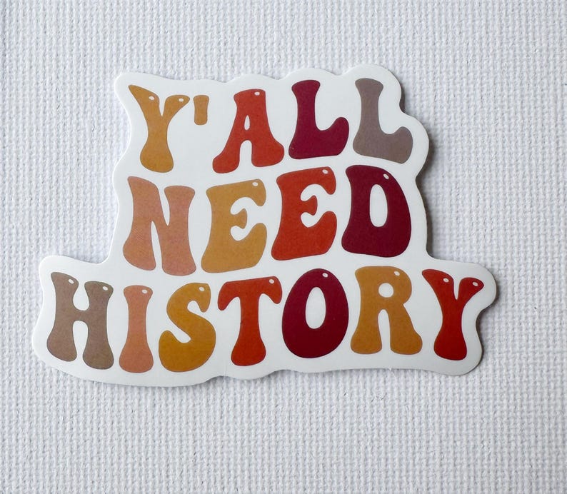 May include: A white sticker with the text "Y'ALL NEED HISTORY" in a retro font. The text is in shades of brown, orange, and red. The sticker has a white border and is on a textured white background.