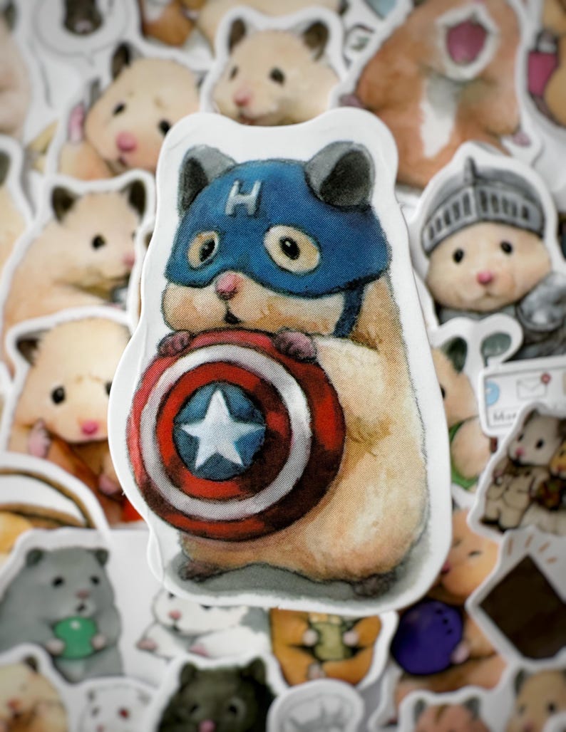 May include: A sticker of a hamster wearing a blue and red Captain America costume, holding a red, white, and blue shield with a white star in the center. The hamster is surrounded by other hamster stickers.