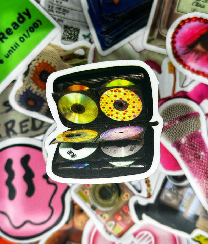 May include: A black CD storage case with a clear plastic cover. The case is open and filled with colourful CDs. The case is a popular way to store and organise CDs.