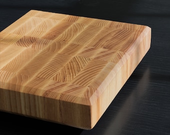 May include: A large, rectangular wooden cutting board with a natural wood grain finish. The board has a slightly rounded edge and is made of solid wood.