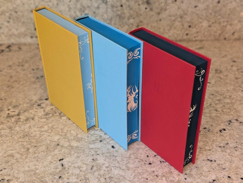 Puede incluir: Tres libros de tapa dura con cubiertas de diferentes colores. El libro de la izquierda es amarillo, el libro del medio es azul claro y el libro de la derecha es rojo.