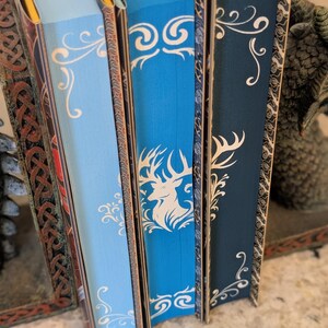 Puede incluir: Cuatro libros de tapa dura con lomos decorativos. Los lomos son azules, azul claro, azul oscuro y rojo. Los libros tienen dise&ntilde;os decorativos blancos en los lomos. Los libros est&aacute;n dispuestos en una fila de izquierda a derecha.