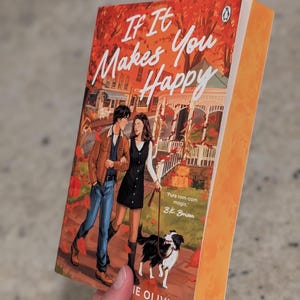 Puede incluir: Un libro de bolsillo titulado "If It Makes You Happy" con una ilustraci&oacute;n de portada de una pareja caminando con un perro. La portada tiene una combinaci&oacute;n de colores naranja y rojo con el nombre del autor, Jamie Olivia, en la parte inferior.