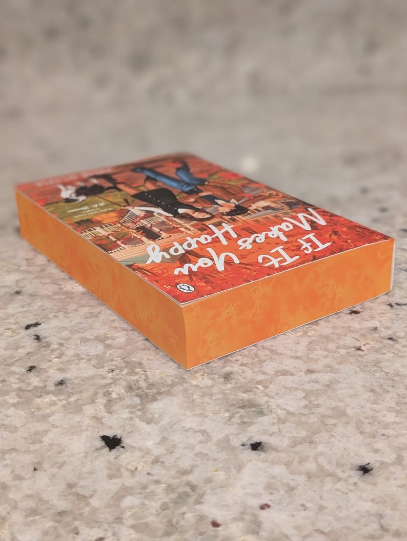 Puede incluir: Un libro de bolsillo titulado "If It Makes You Happy" con una cubierta y lomo naranja. La cubierta presenta una ilustraci&oacute;n colorida de personas y edificios. El logotipo de Penguin es visible. El libro est&aacute; sobre una superficie moteada.