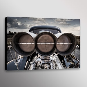 May include: A close-up of a custom-built hot rod engine with three large, round, polished intake manifolds. The engine is silver and chrome with black accents. The background is a blurry image of a cloudy sky and a paved road.