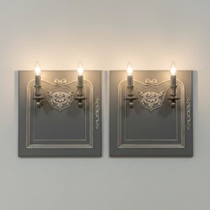 Peut inclure: Deux appliques murales grises avec des détails décoratifs et des ampoules en forme de bougie. Chaque applique présente un design rectangulaire avec une bordure ornée et un élément décoratif central. Les appliques sont montées sur un mur blanc.