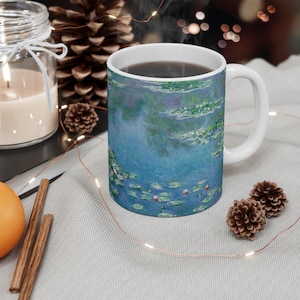 Puede incluir: Una taza de cer&aacute;mica blanca con un dise&ntilde;o azul y verde de nen&uacute;fares. La taza est&aacute; llena de caf&eacute; y tiene un asa blanca.