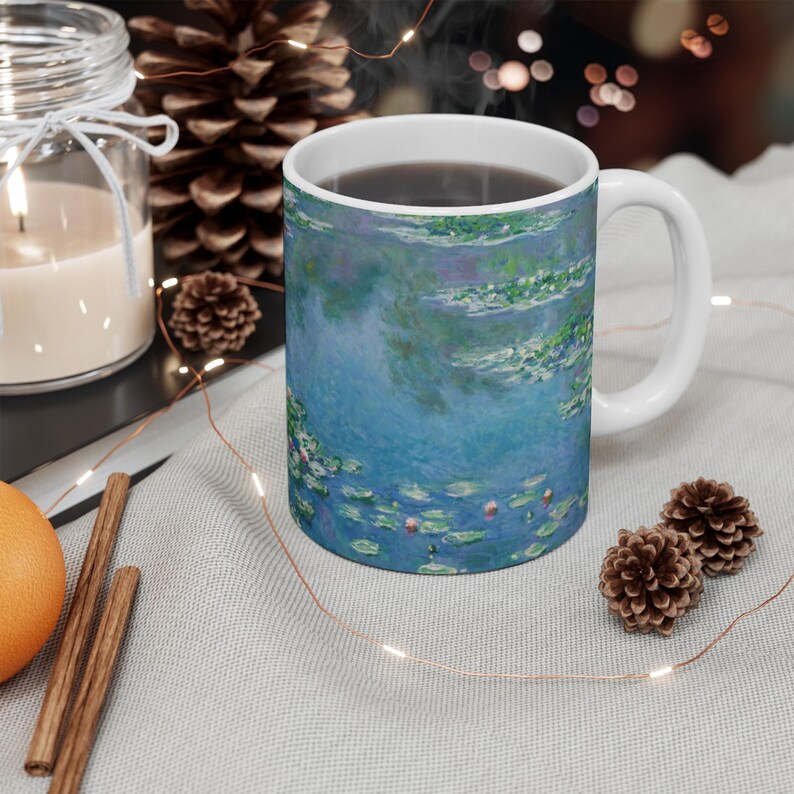 Puede incluir: Una taza de cer&aacute;mica blanca con un dise&ntilde;o azul y verde de nen&uacute;fares. La taza est&aacute; llena de caf&eacute; y tiene un asa blanca.