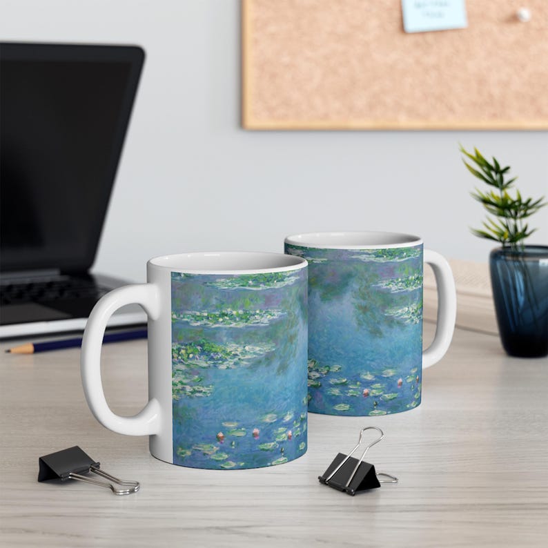 Puede incluir: Dos tazas de cer&aacute;mica blanca con un dise&ntilde;o de nen&uacute;fares azul y verde. Las tazas est&aacute;n sobre una superficie de madera clara.