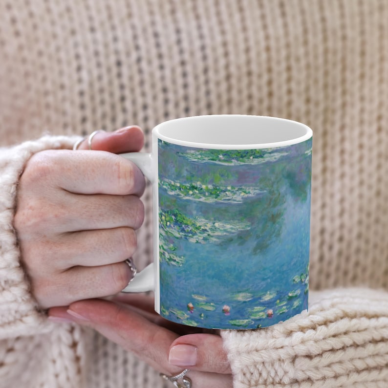 Puede incluir: Taza de cer&aacute;mica blanca con una pintura de acuarela azul y verde de nen&uacute;fares. La pintura recuerda el estilo impresionista de Claude Monet.